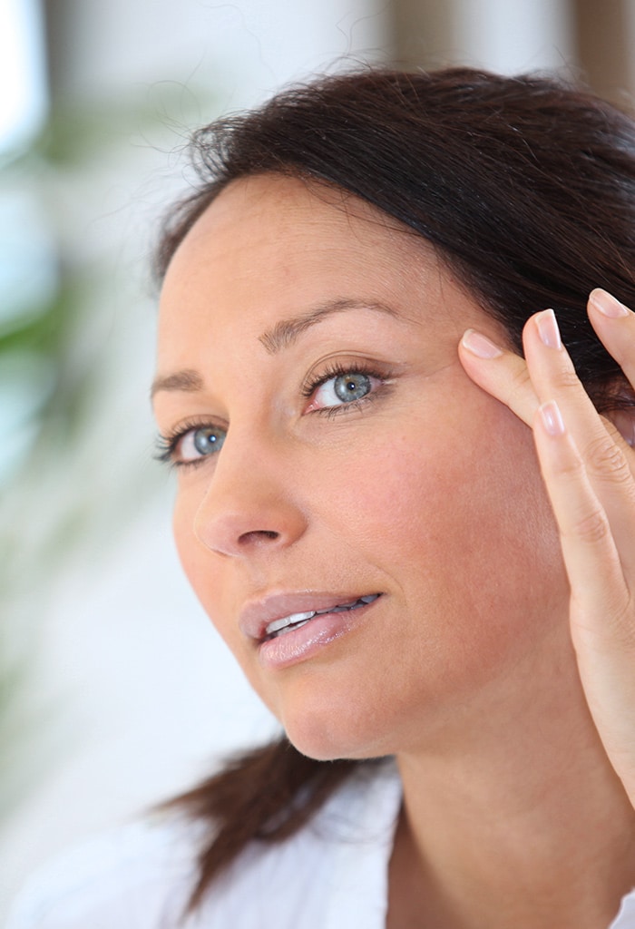 Woman with blue eyes looking her skin in the mirror